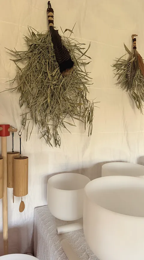 The studio: white crystal singing bowls, wooden wind chimes and bundles of dried herbs against a soft white drape